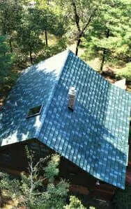 Blue solar panel roof on house surrounded by green trees and forest canopy