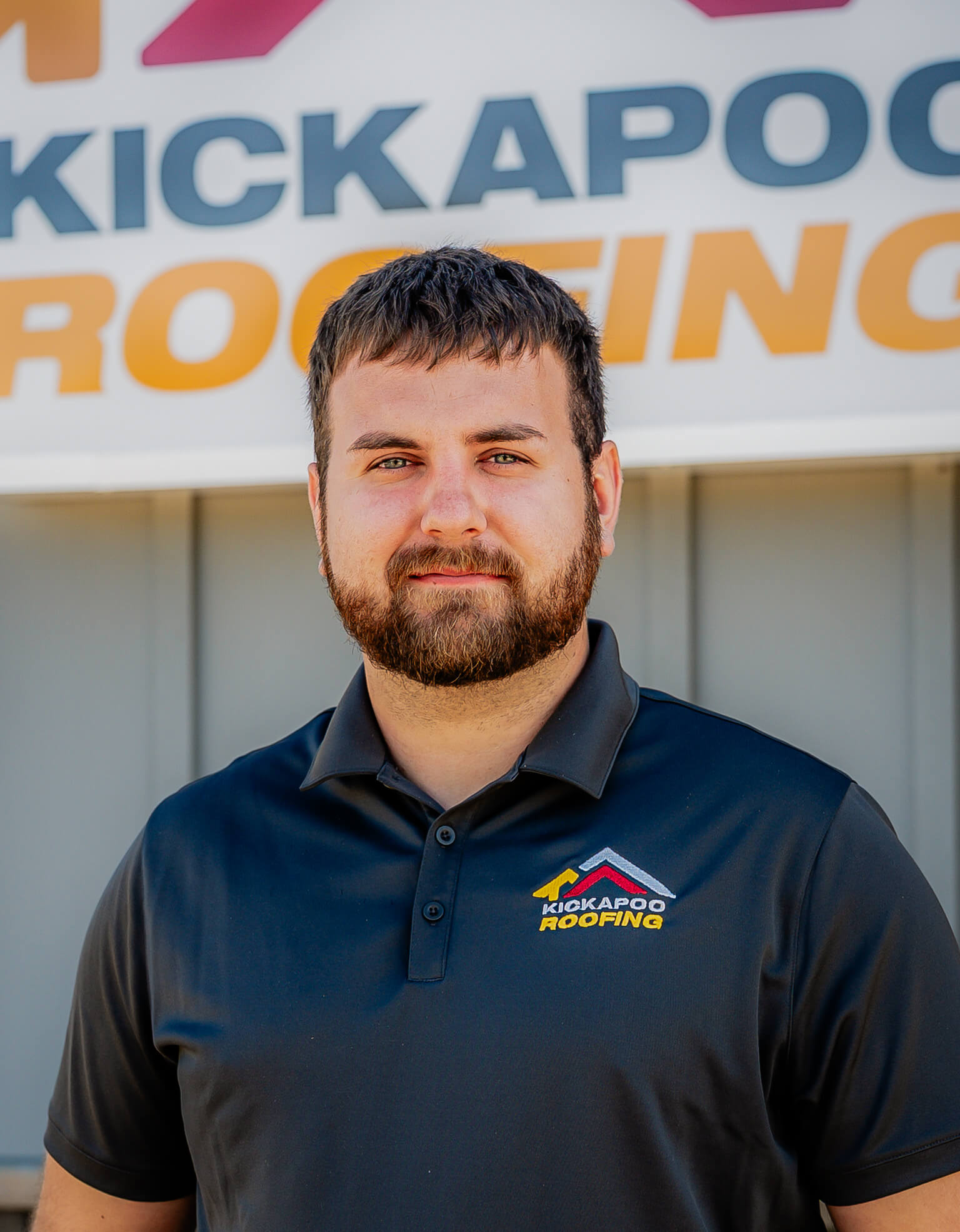 Professional man with beard wearing Kickapoo Roofing polo shirt smiling outdoors