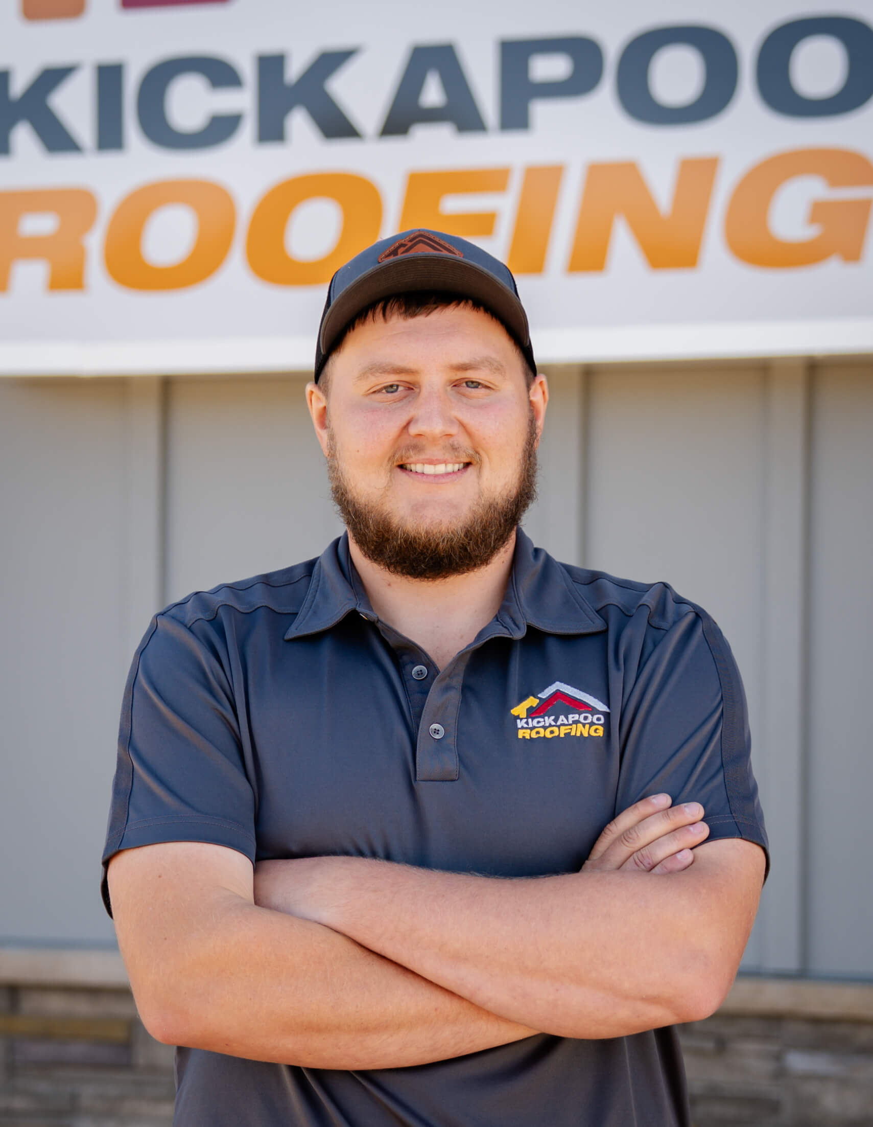 Smiling Kickapoo Roofing employee in navy polo shirt with crossed arms