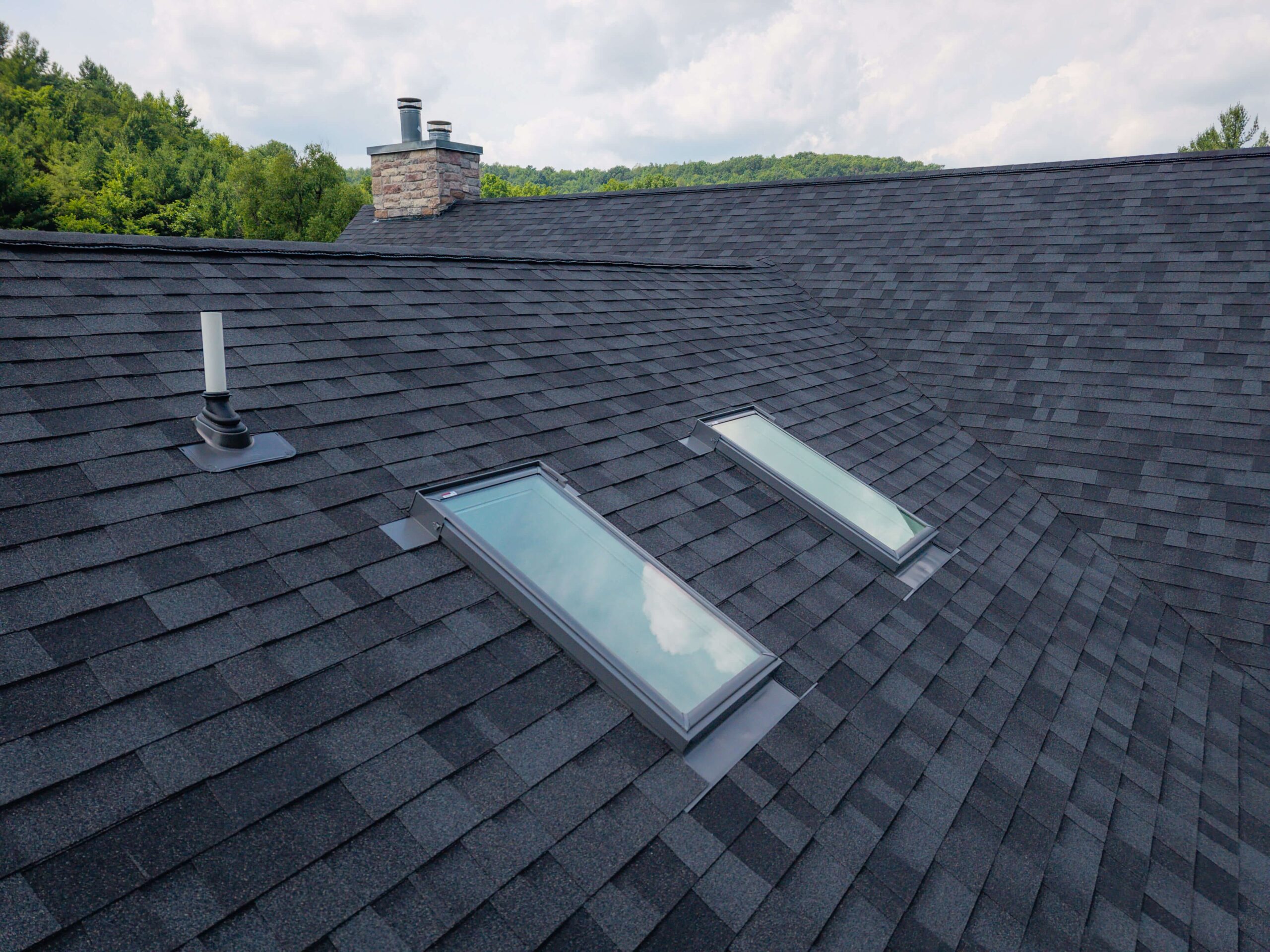 Dark gray asphalt shingle roof with two skylights and stone chimney