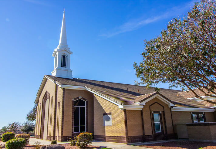 Exterior view of a brick church with white steeple under a clear blue sky.