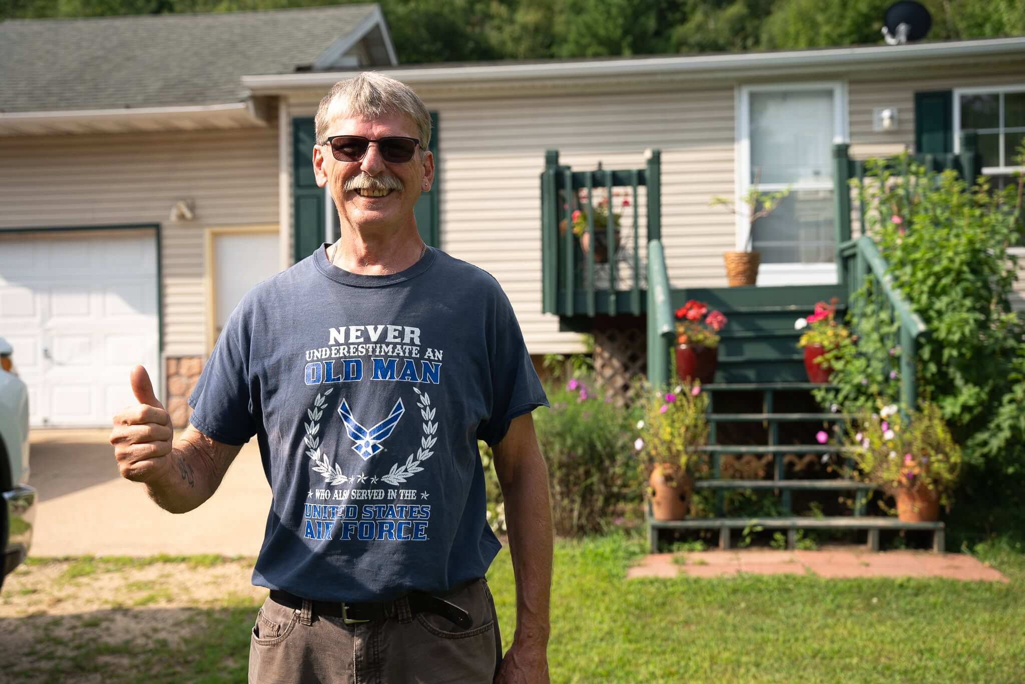 Man with sunglasses smiling and giving thumbs up in front of house